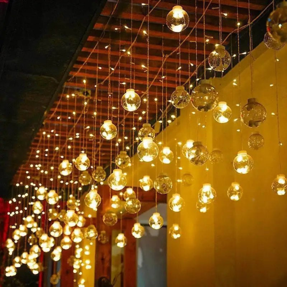 Cortina luminosa con bolas colgantes — ambiente cálido y festivo