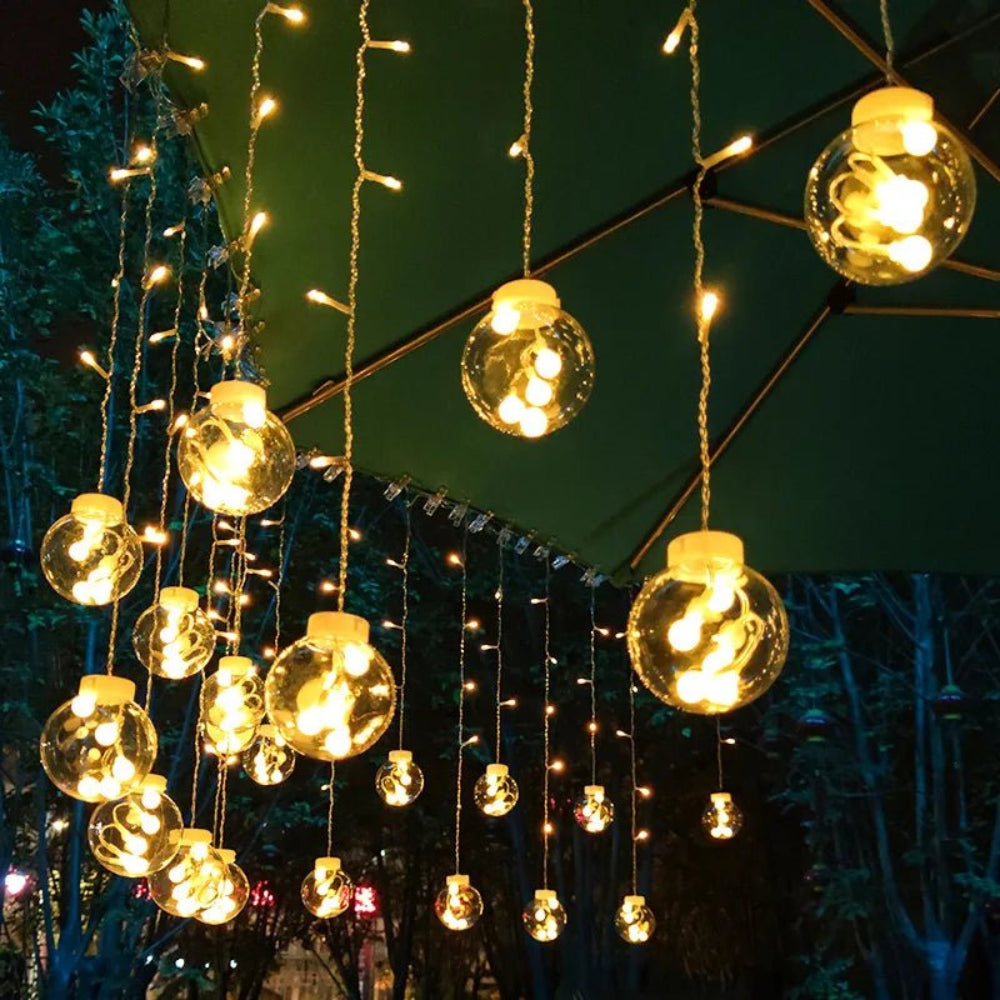 Cortina luminosa con bolas colgantes — ambiente cálido y festivo 