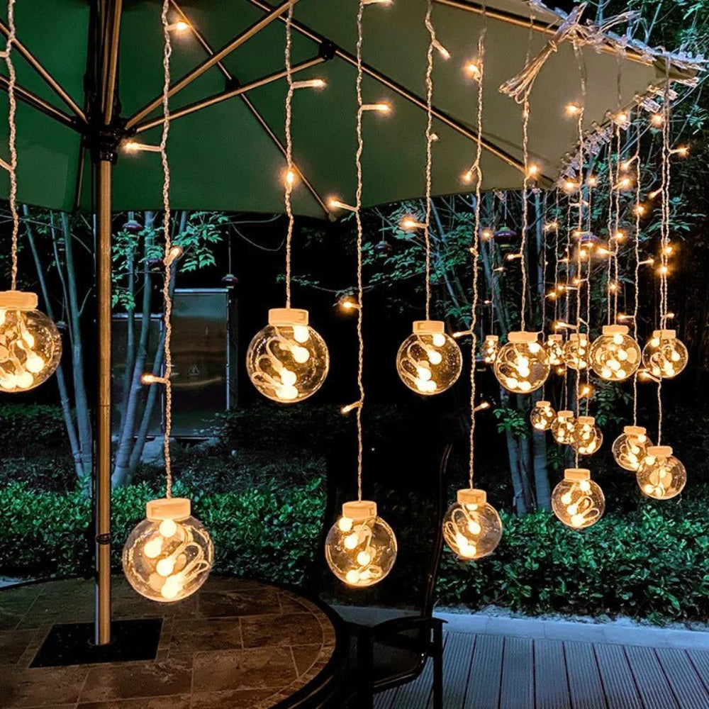 Cortina luminosa con bolas colgantes — ambiente cálido y festivo 